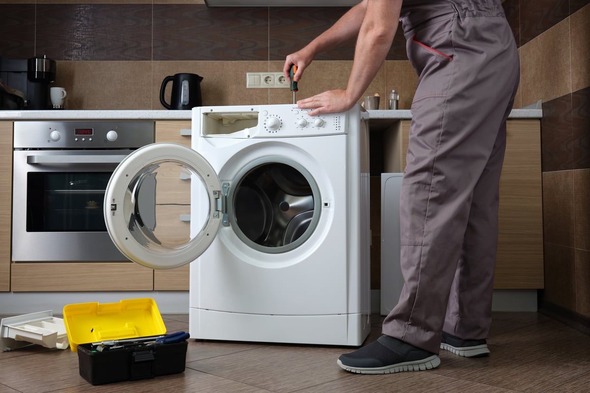 A adult household appliance repairman disassembling a washing machine with a screwdriver. Professional repair of household appliances.