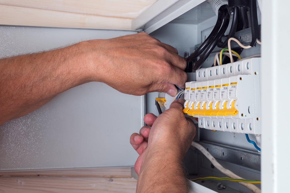 Electrician's hands skillfully connecting cables in an open distribution board, focusing on quality and precision for safe power usage.