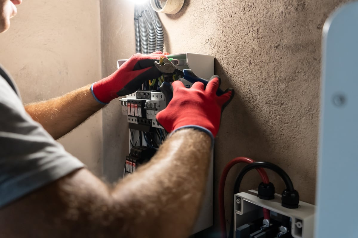 Electrician performing maintenance or installation work inside an electrical panel, ensuring safety and proper electrical connection.
