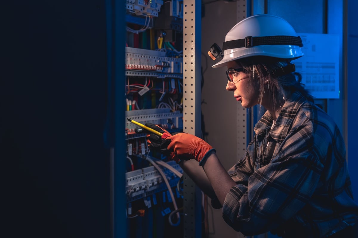 A woman engineer in a hard hat headlamp works near terminals and breakers using insulated tools. Blue shadows with warm highlights create a cinematic safety focused maintenance mood.